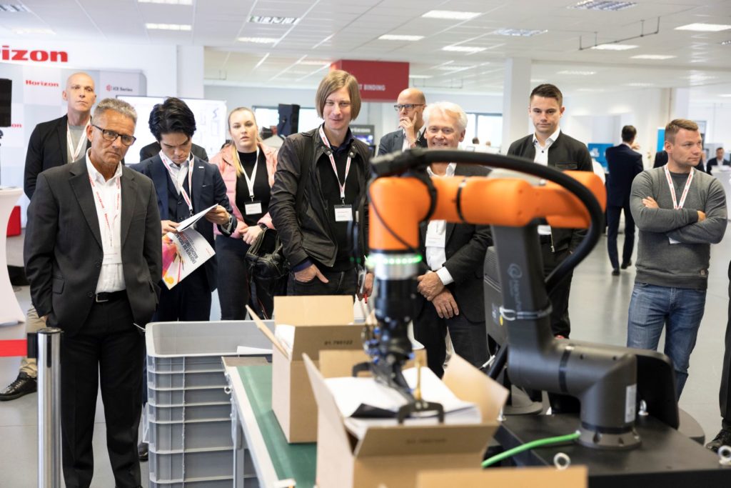 Mithilfe eines Kartonierroboters werden die gehefteten und banderolierten Broschüren in Kartons verpackt. Foto: Horizon GmbH